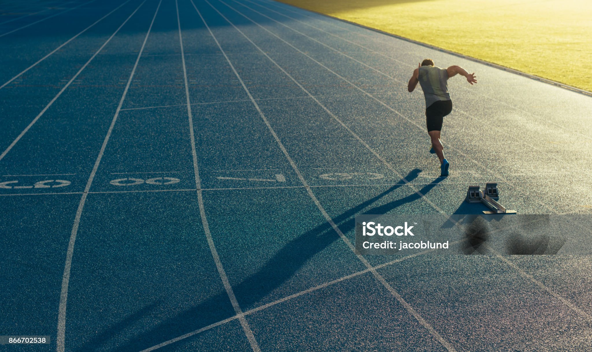 Athlete running on an all-weather running track alone. Runner sprinting on a blue rubberized running track starting off using a starting block.